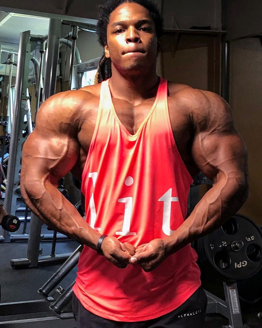 Jay Coss flexing his huge, ripped, and broad shoulders in a red tank top