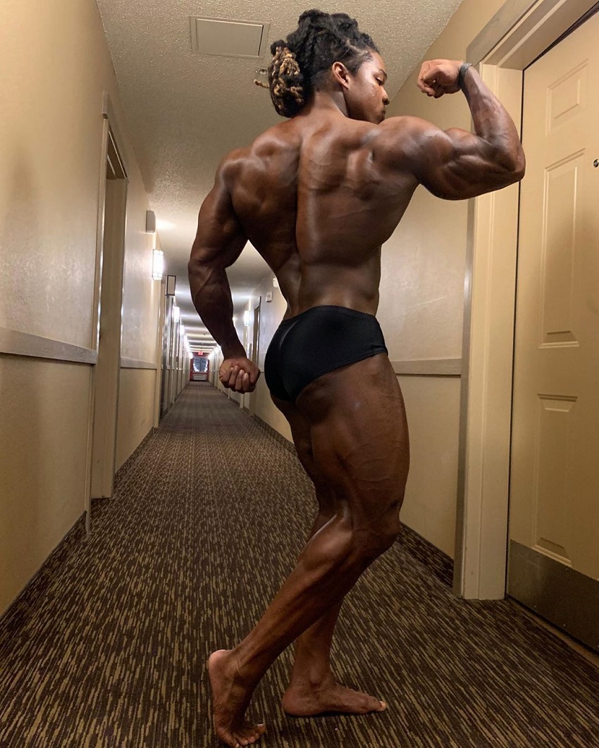 Jay Coss flexing his biceps and back in a hotel corridor