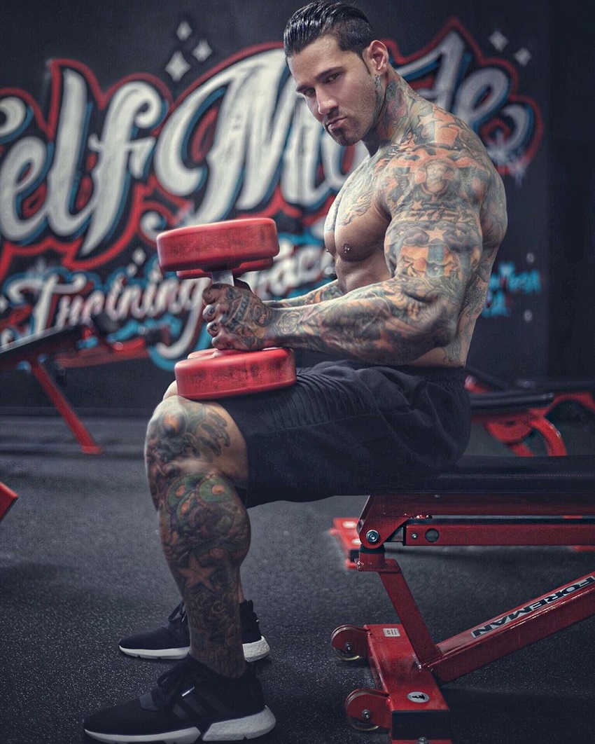 Michael Giovanni Rivera sitting on a bench with two red dumbbells in each hand