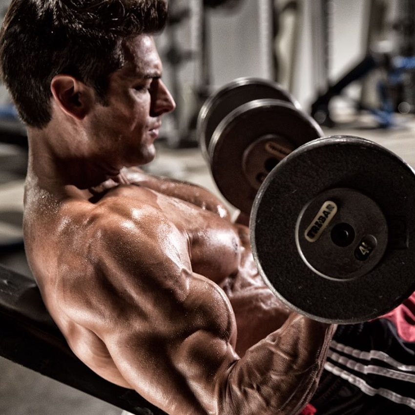 Shirtless TJ Hoban doing biceps curls shirtless in the gym