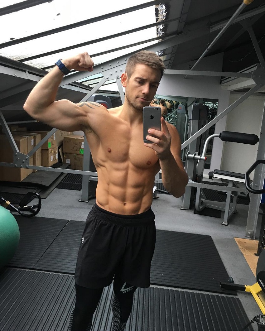 Alex Crockford flexing his biceps shirtless in the gym