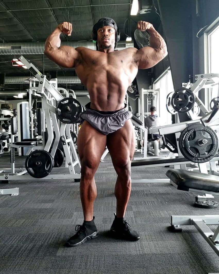 Rickey Moten flexing front double biceps shirtless in the gym