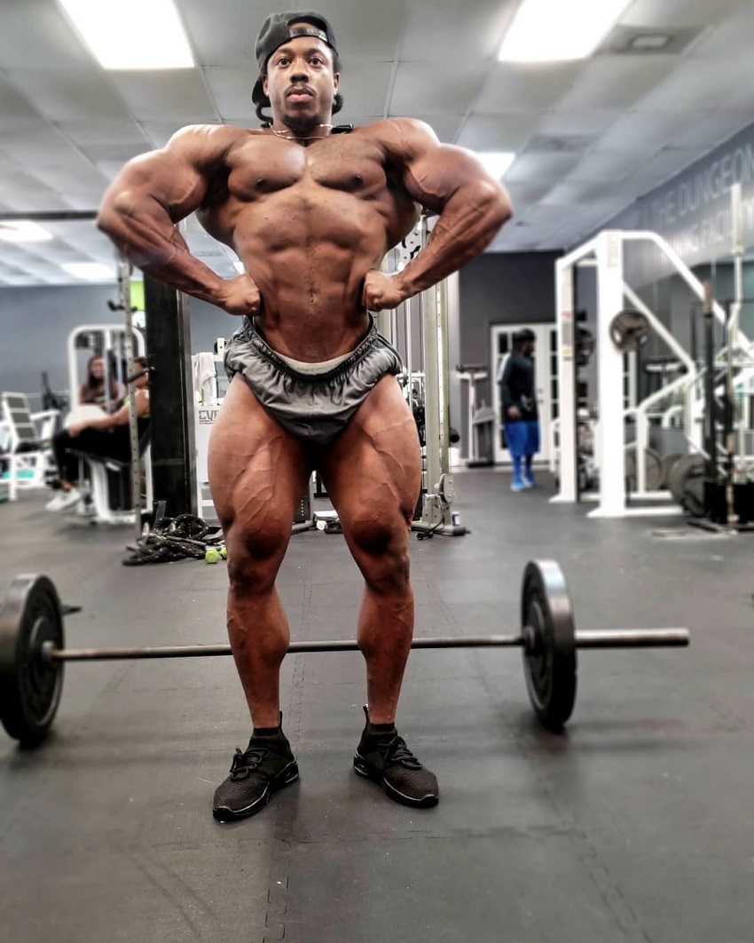 Rickey Moten posing front lat spread shirtless in the gym