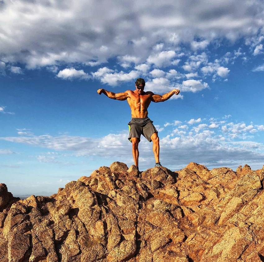 Brandon Budlong posing shirtless on top of a mountain