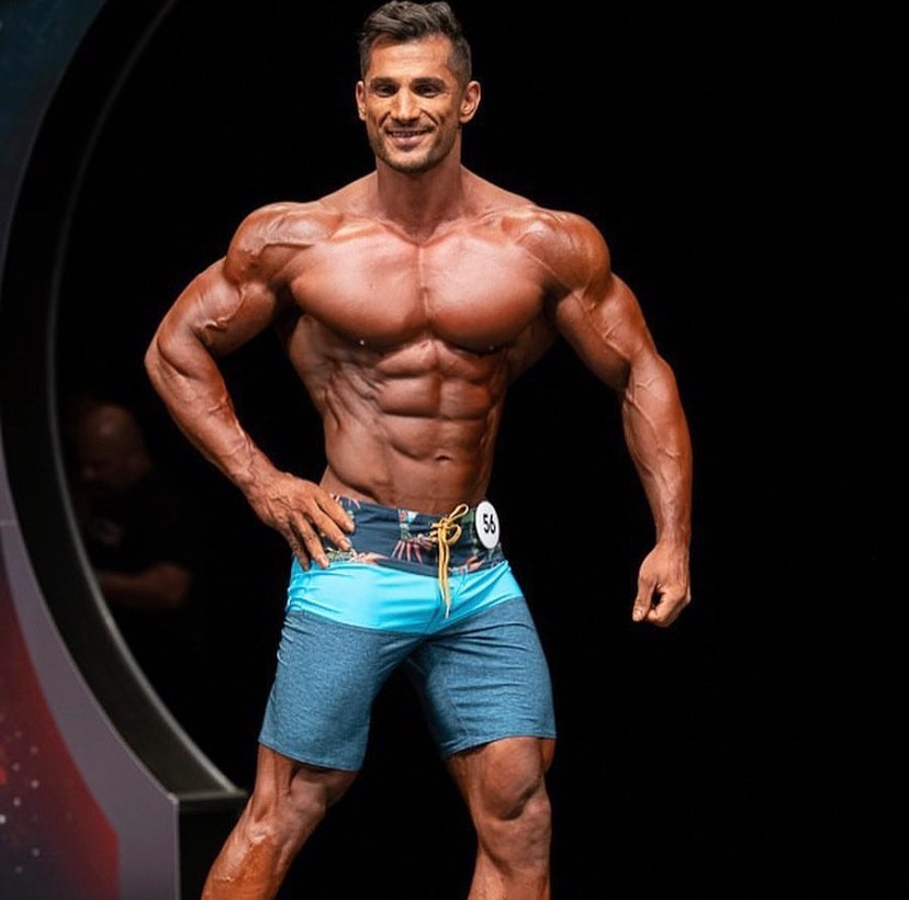 Akbar Sarbaz flexing his ripped physique in front of the audience in a bodybuilding competition