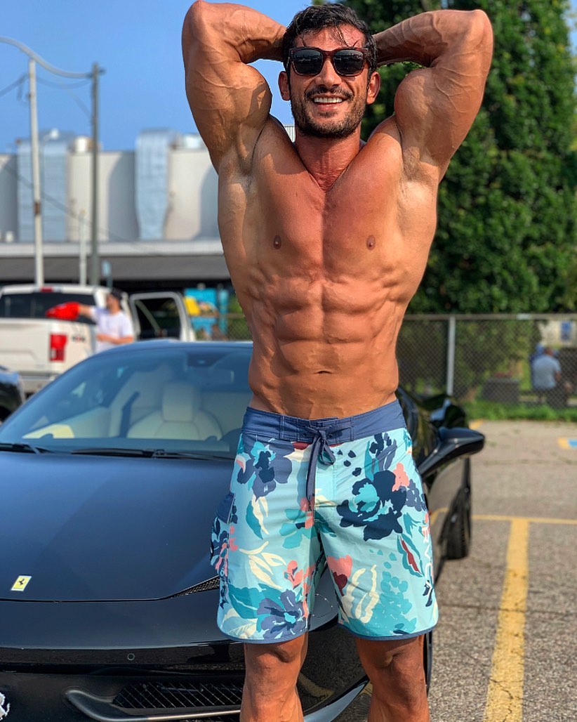 Akbar Sarbaz flexing his ripped abs beside a ferrari