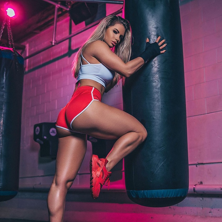 Amy Lee leaning against a boxing bag looking curvy fit and lean