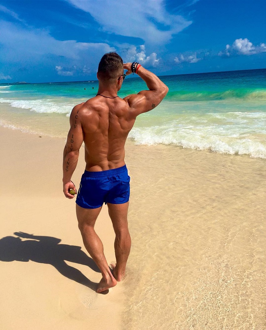 Bryan McCormick standing shirtless on a beach looking ripped