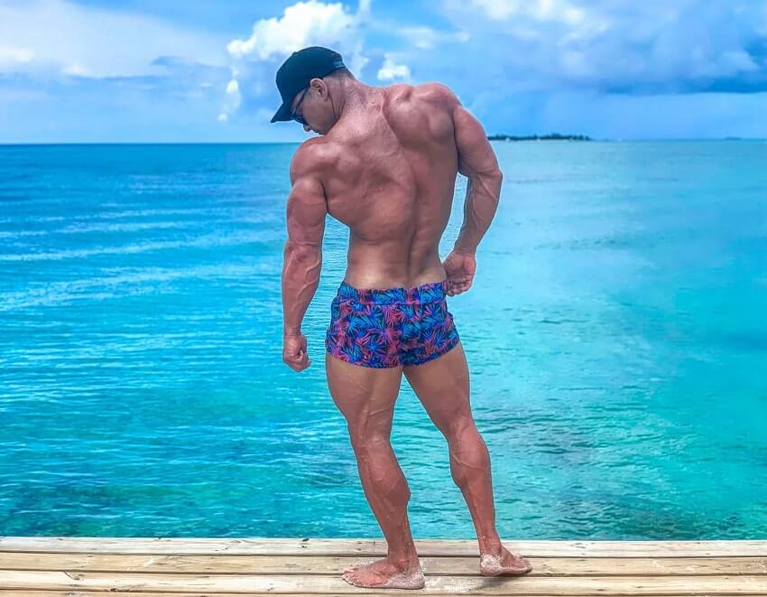 Dan Mazzola flexing his back and triceps by the sea