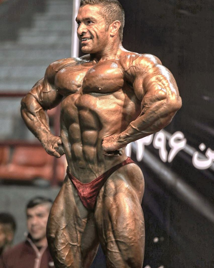 Majid Jameh Bozorg posing on a bodybuilding stage, looking incredibly ripped and huge