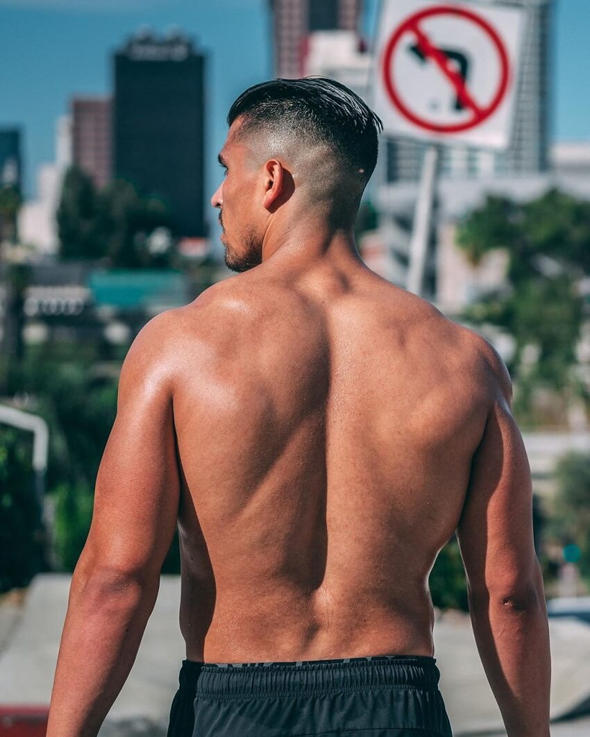 Garret Fisher strolling shirtless down the beach, with his back looking wide and muscular