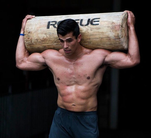 Garret Fisher shirtless, carrying heavy log over his head