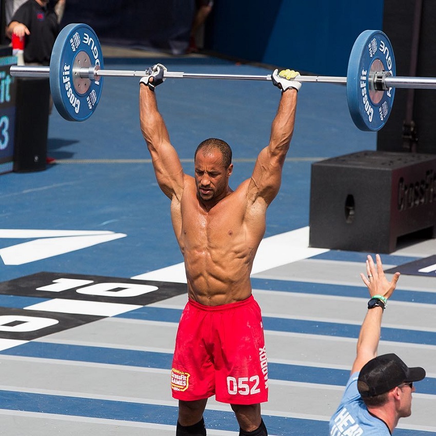 Neal Maddox shirtless, doing overhead barbell press during CrossFit Games